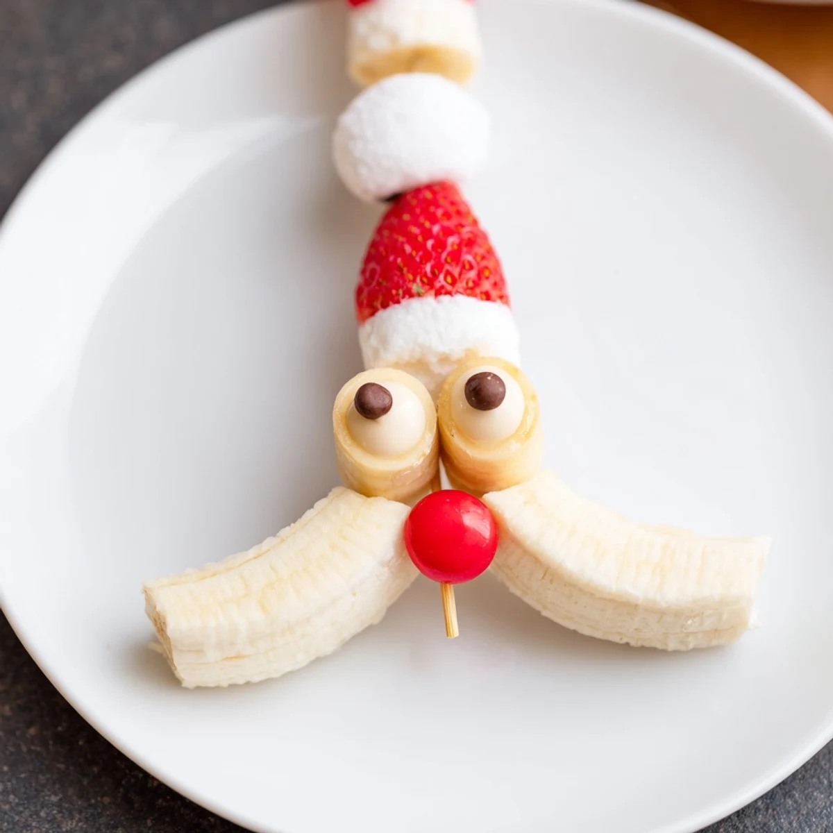 Festive Banana Santa Snack Sticks skewer: a cheerful dessert of banana faces topped with strawberry hats.