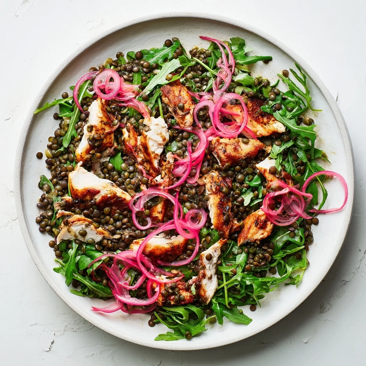 Freshly tossed Lentil & Chicken Spring Salad in a white bowl, with pickled red onions, cherry tomatoes, and a light vinaigrette glazing the greens.