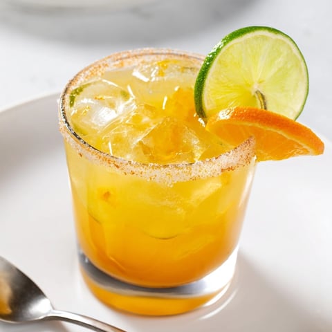 Close-up of a chilled Tangerine Margarita in a salt-rimmed glass, garnished brightly.