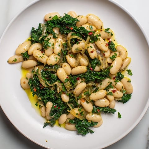 Steaming bowl of Garlicky Beans with Winter Greens, featuring vibrant greens and creamy cannellini beans.