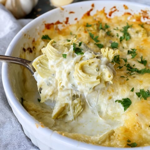 A bubbly Baked Artichoke Dip with golden cheese crust, perfect for dipping with crackers.