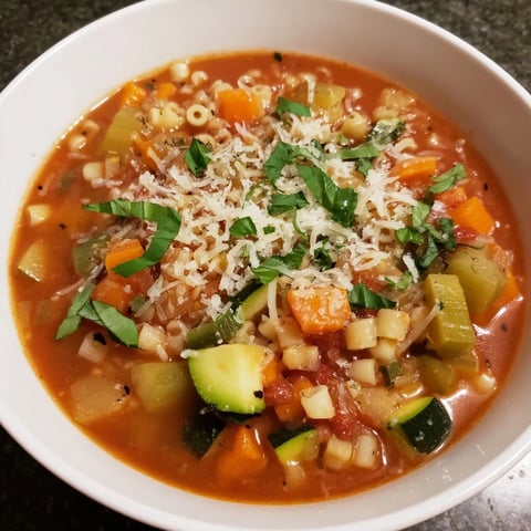 Steaming bowl of tomato basil minestrone, filled with vegetables and pasta, perfect for dinner.