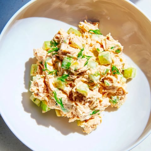 A close-up of Spicy Zesty Tuna Salad garnished with fresh parsley and lemon wedges on a rustic plate.