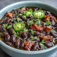 A steaming bowl of Black Bean and Ham Soup with jalapeños, topped with fresh cilantro and lime wedges.
