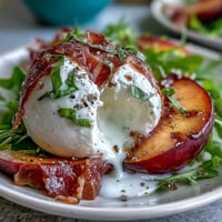 Creamy burrata and juicy peaches atop fresh greens, drizzled with balsamic glaze and paired with salty prosciutto.